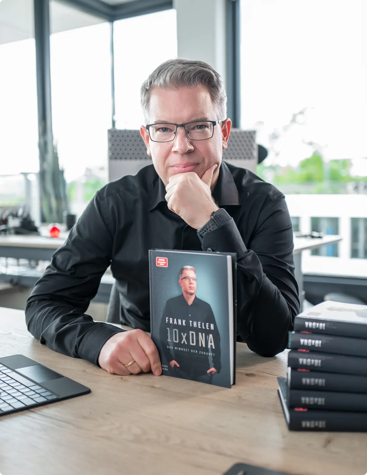 Frank Thelen, deep-tech investor and author of '10xDNA', posing with his book at a desk in an office setting.